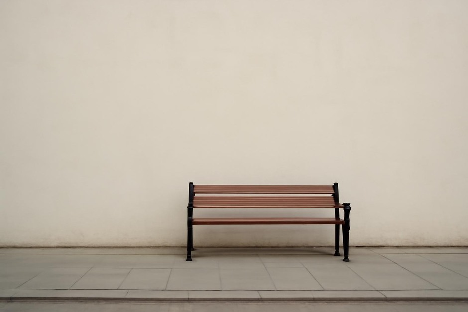 A lone bench against an expanse of pale wall